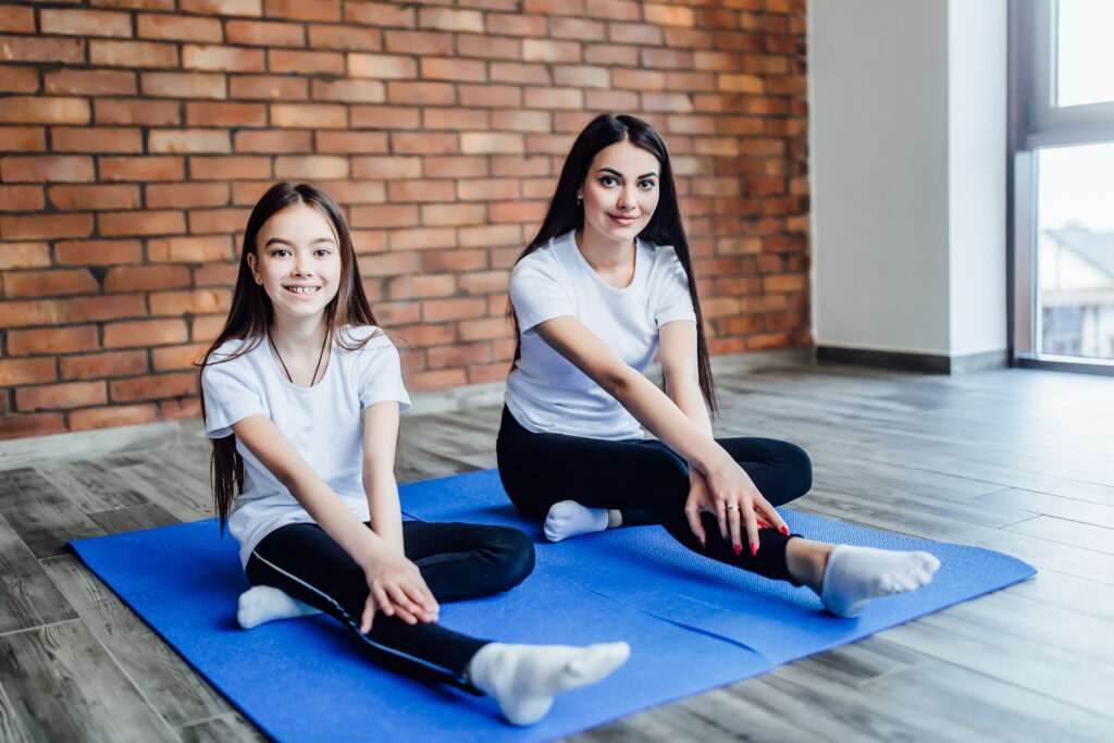 Mother and daughter practicing yoga in butterfly pose at home.