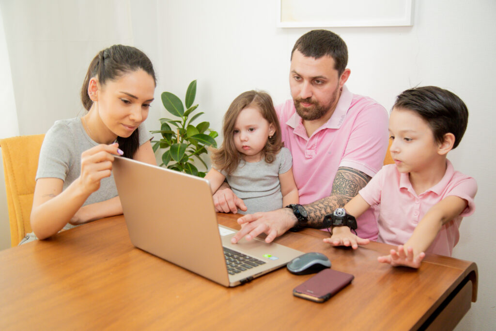 Happy Loving Family with Little Cute Children Sitting together: Father working on Laptop at Home
