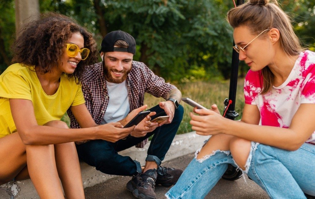 Happy young company smiling friends Sitting in Park-grass with Electric Scooter having fun together Positive and Negative Impacts of Social Media on Youth